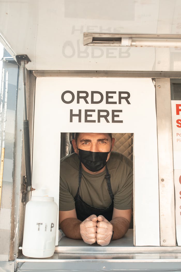 A food truck vendor wearing a mask, ready to take orders through a window.